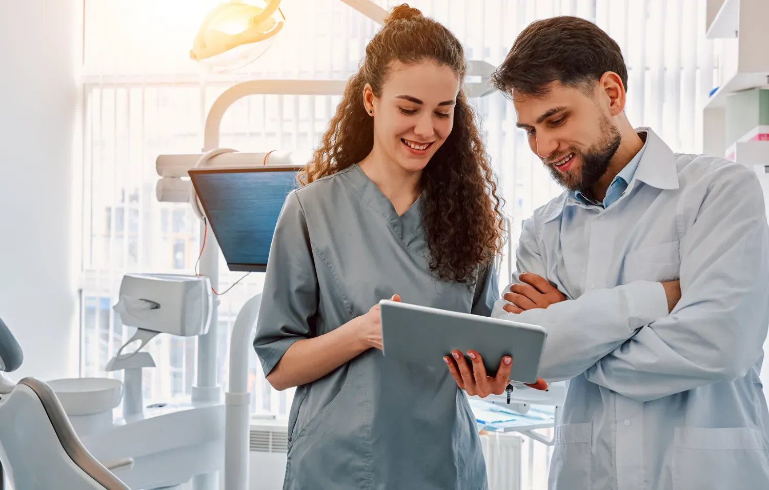 A dental professional and a hygienist review information on a tablet while standing in a modern dental office.